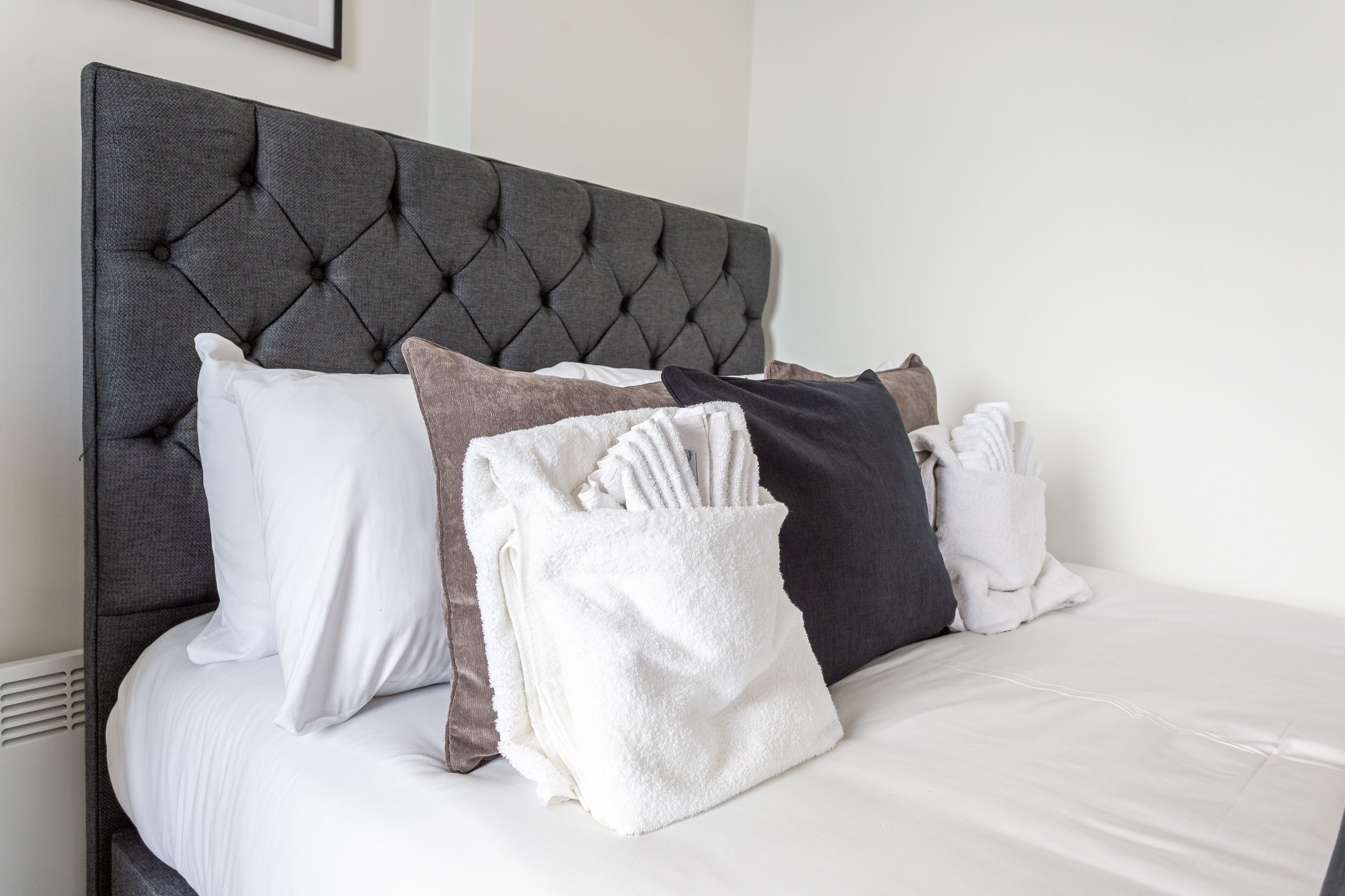 A neatly made bed with a tufted headboard, white and brown pillows, and a white towel with utensils.