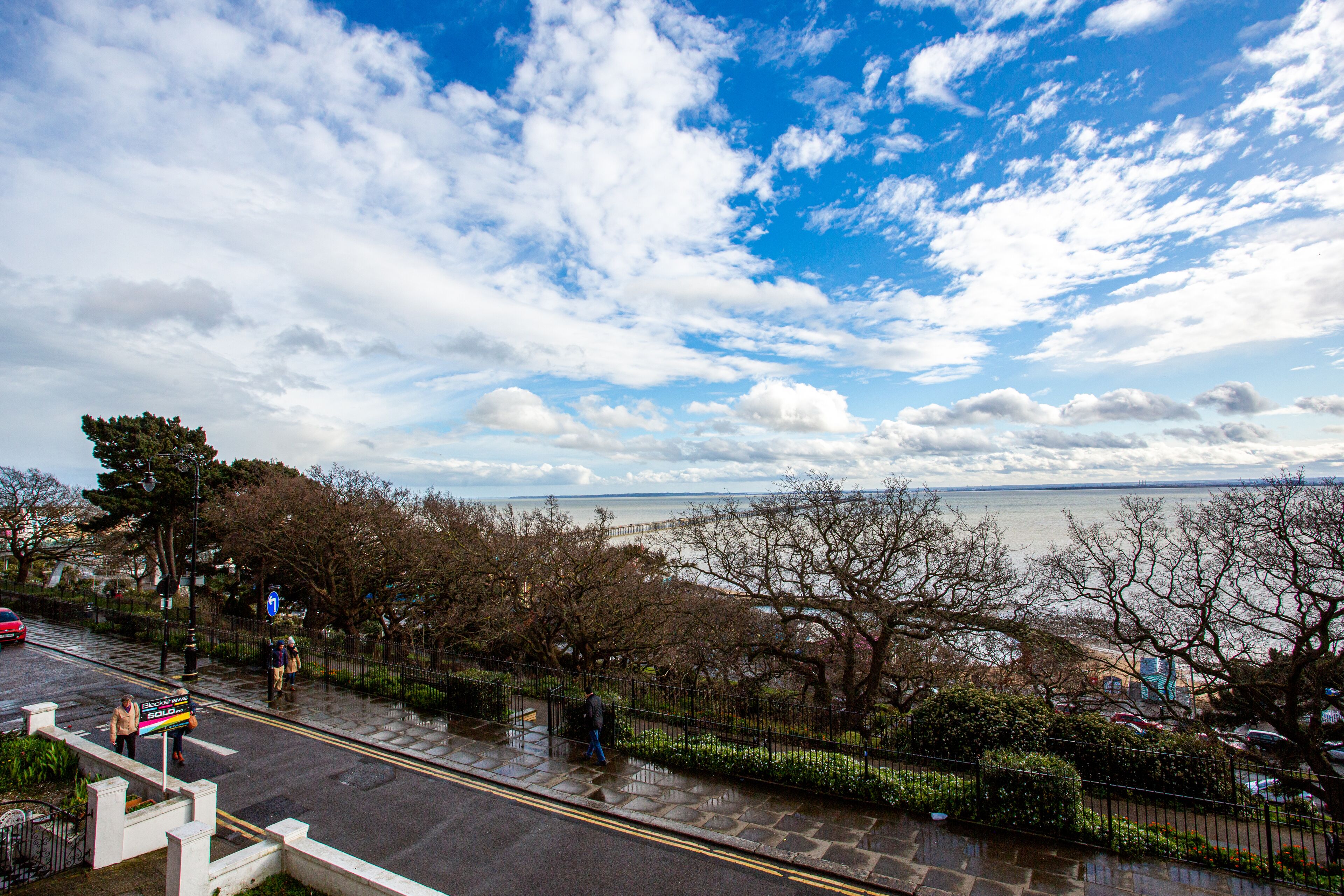 A coastal road with a pedestrian path, a bridge, and a view of the sea.