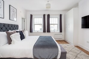 A modern bedroom with a large bed, a flat-screen TV, and a window with curtains.