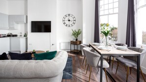 A modern kitchen with white cabinets, a flat-screen TV, and a dining area with a wooden table and chairs. - The Regency Apartments (Southend-on-Sea)
