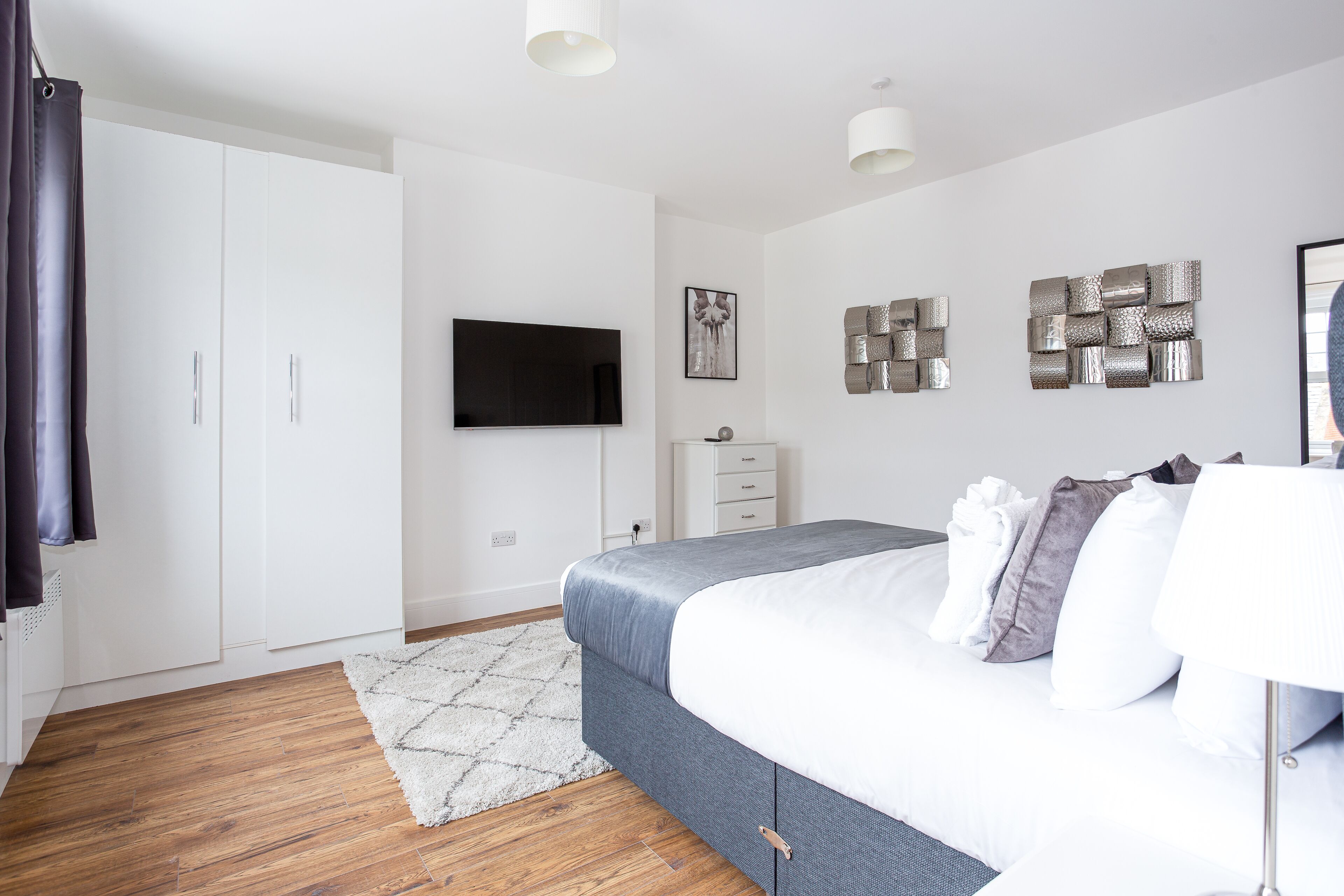 Une chambre moderne comprenant un lit, un téléviseur à écran plat, une armoire et des œuvres d’art décoratives au mur.