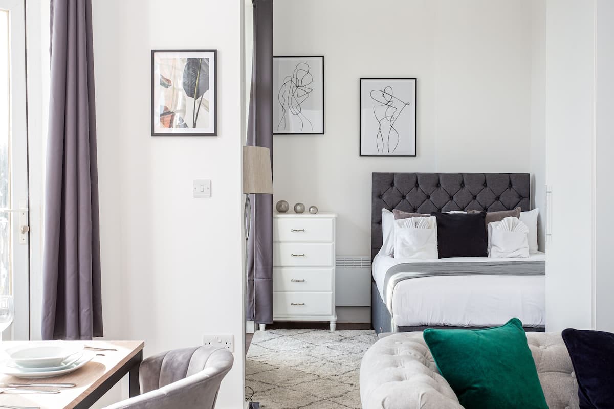 A modern bedroom with a tufted headboard bed, a white dresser, and abstract wall art.