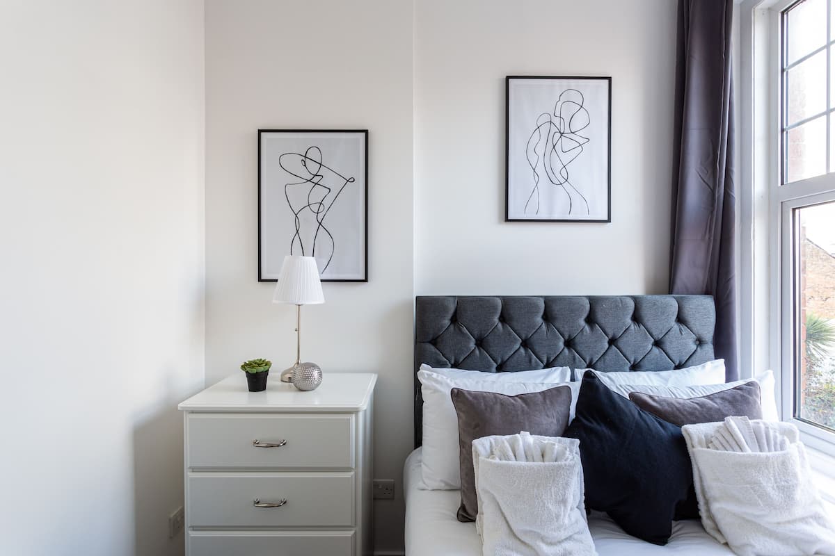 A bedroom with a tufted headboard, a bedside table with a lamp, and artwork on the wall.
