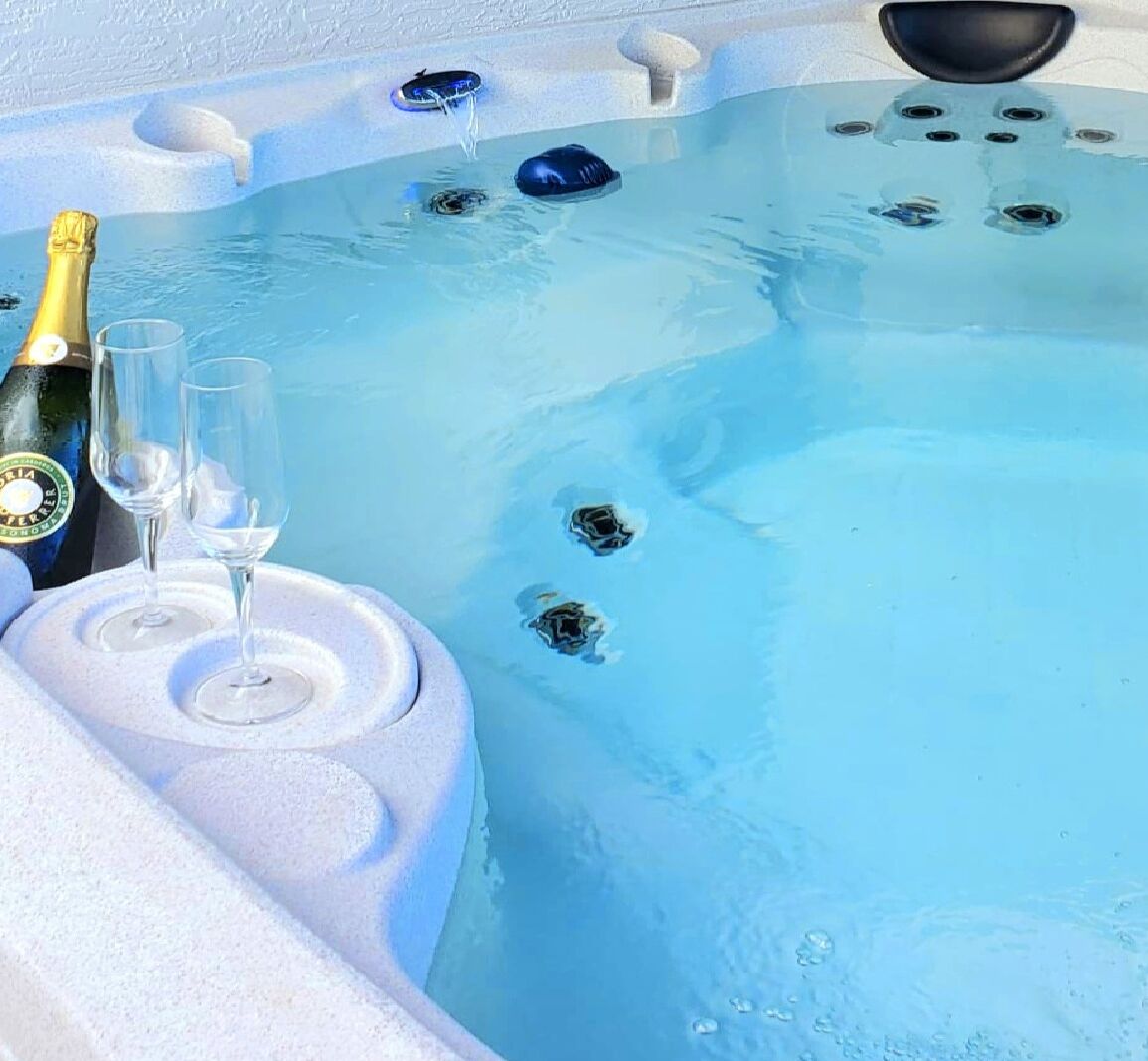 A hot tub with two champagne glasses and a bottle, surrounded by bubbles.