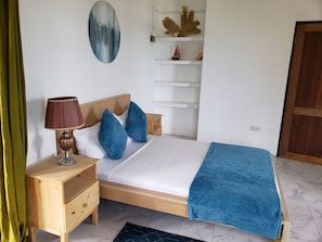 A bedroom with a wooden bed, a nightstand with a lamp, a blue blanket, and a wall with a decorative piece.