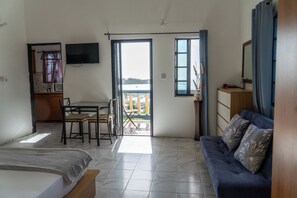 Una habitación con cama, sofá, mesa de comedor con sillas, televisor montado en la pared y balcón con vistas.