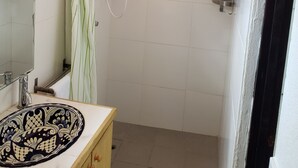 Een badkamer met een douche, een wastafel met decoratieve wasbak, een spiegel en een handdoekrek.