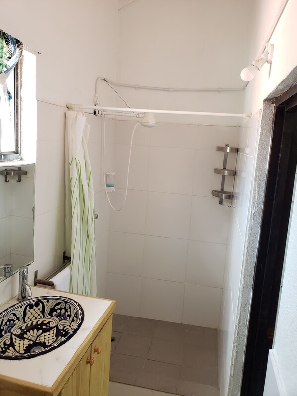 Een badkamer met een douche, een wastafel met decoratieve wasbak, een spiegel en een handdoekrek.