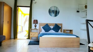 Een slaapkamer met een houten bed, een nachtkastje, een lamp, een ronde wanddecoratie en uitzicht buiten door een deur.