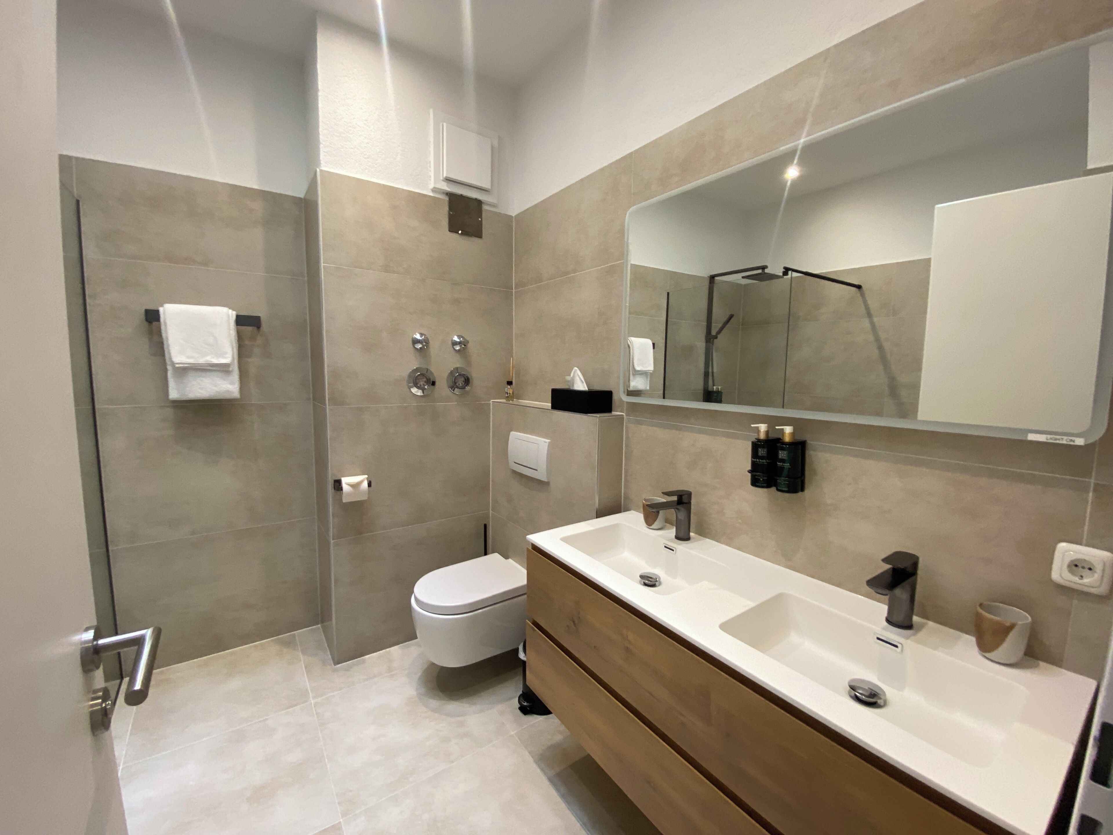 Ein modernes Badezimmer mit Dusche, Toilette, Waschtisch und einem großen Spiegel.