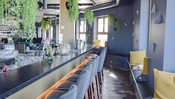 Eine moderne Bar mit einer langen Theke, Barhocker und hängenden Pflanzen.