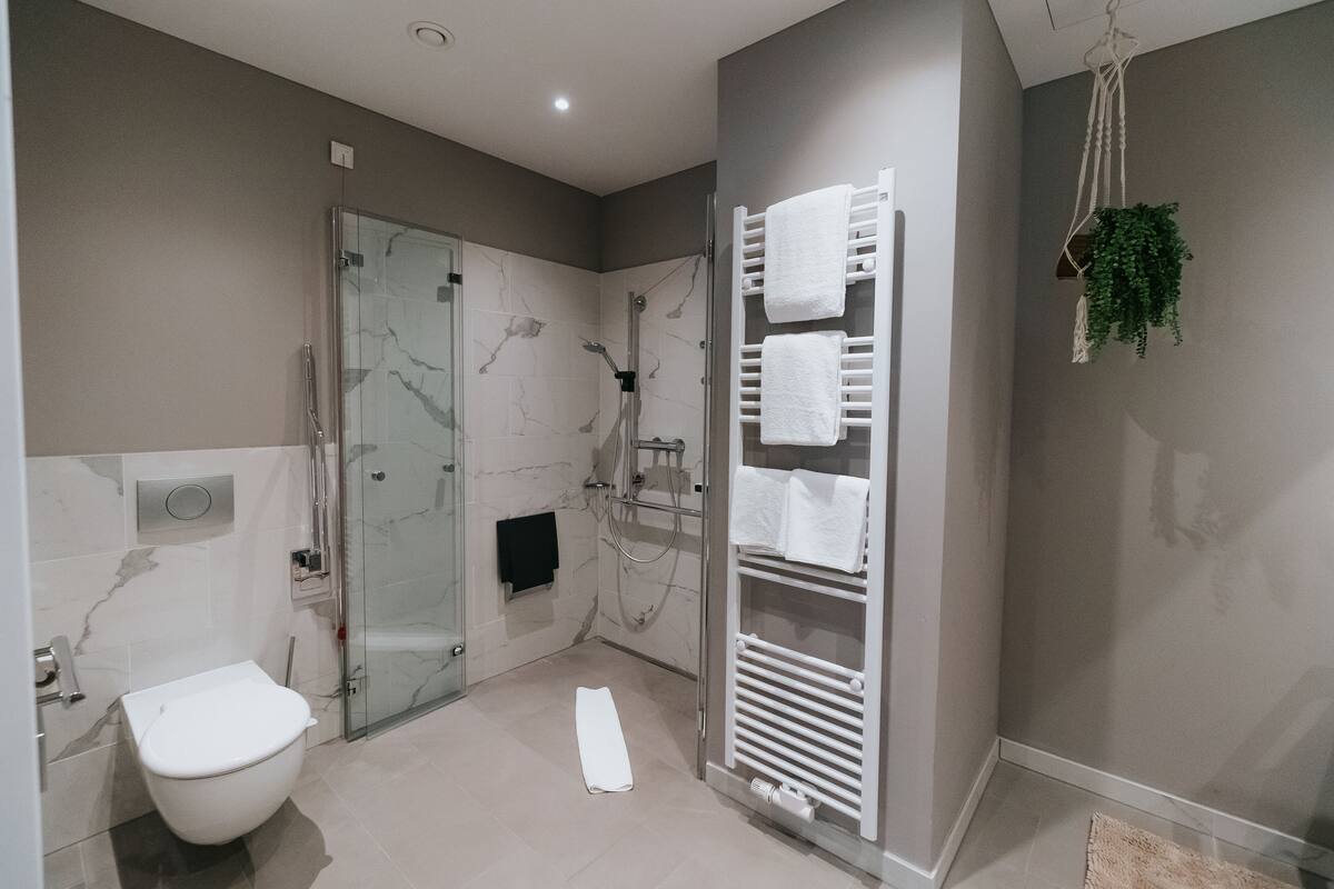 A modern bathroom with a glass-enclosed shower, a white toilet, and a towel rack with multiple towels.