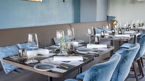 Un restaurante con varias mesas dispuestas para comer, con sillas tapizadas en azul y una presentación de mesas ordenada.
