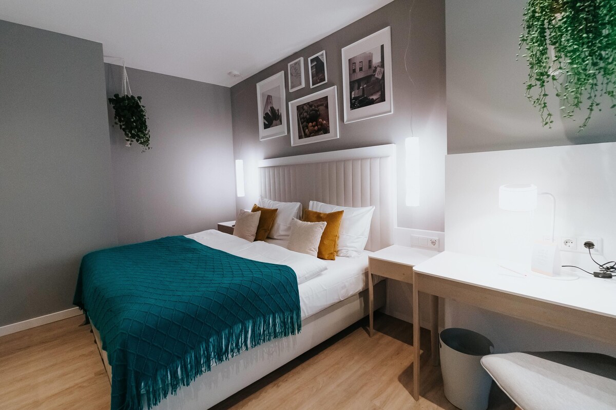 A modern bedroom with a bed, bedside table, and a desk with a chair.