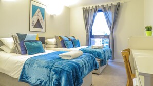 A hotel room with two beds, a desk, and a window with curtains. - Tudors eSuites Birmingham Apartments with Parking (Birmingham)