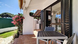 Un patio con una mesa y sillas, una puerta corrediza de vidrio y una valla verde al fondo.