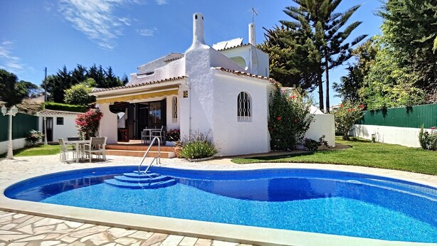 Una casa con piscina, un patio con sillas y un pequeño jardín.