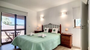 Un dormitorio con una cama, dos mesitas de noche, una ventana y una puerta.