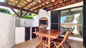An outdoor kitchen with a brick oven, a wooden table, and chairs.