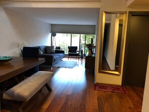 A modern living room with a dining area, a sofa, a bench, and a view through a large window.