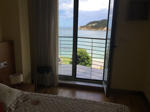 Une chambre d’hôtel avec un lit, une chaise, un bureau et une fenêtre donnant sur la mer et une colline.