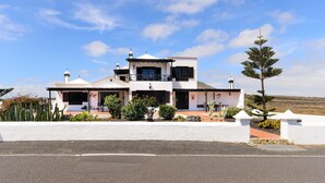 A two-story building with a white facade, multiple windows, and a flat roof. - Clara Suite 1: Large Pool, Spectacular Views, Terrace, Garden & Wi-Fi (Lanzarote)