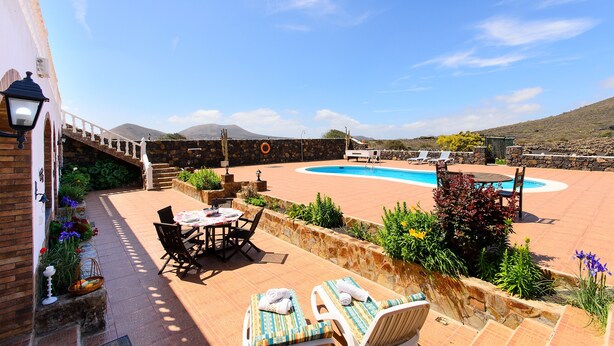 A patio with a pool, outdoor furniture, and a stone wall. - Clara Suite 1: Large Pool, Spectacular Views, Terrace, Garden & Wi-Fi (Lanzarote)