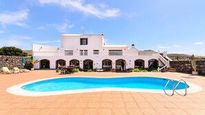 A large building with a swimming pool, outdoor seating, and a staircase leading to the entrance. - Clara Suite 1: Large Pool, Spectacular Views, Terrace, Garden & Wi-Fi (Lanzarote)