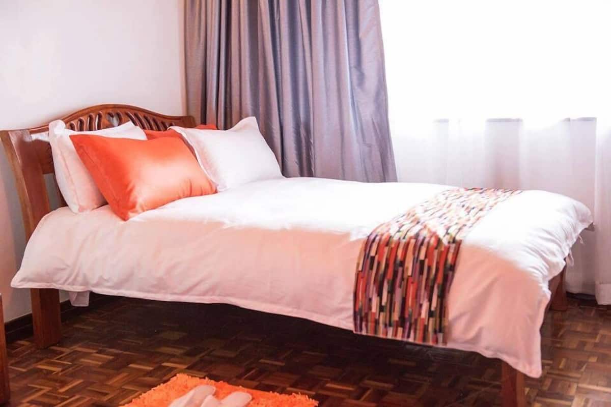 A neatly made bed with a white and orange bedding set, a wooden headboard, and a patterned throw blanket.