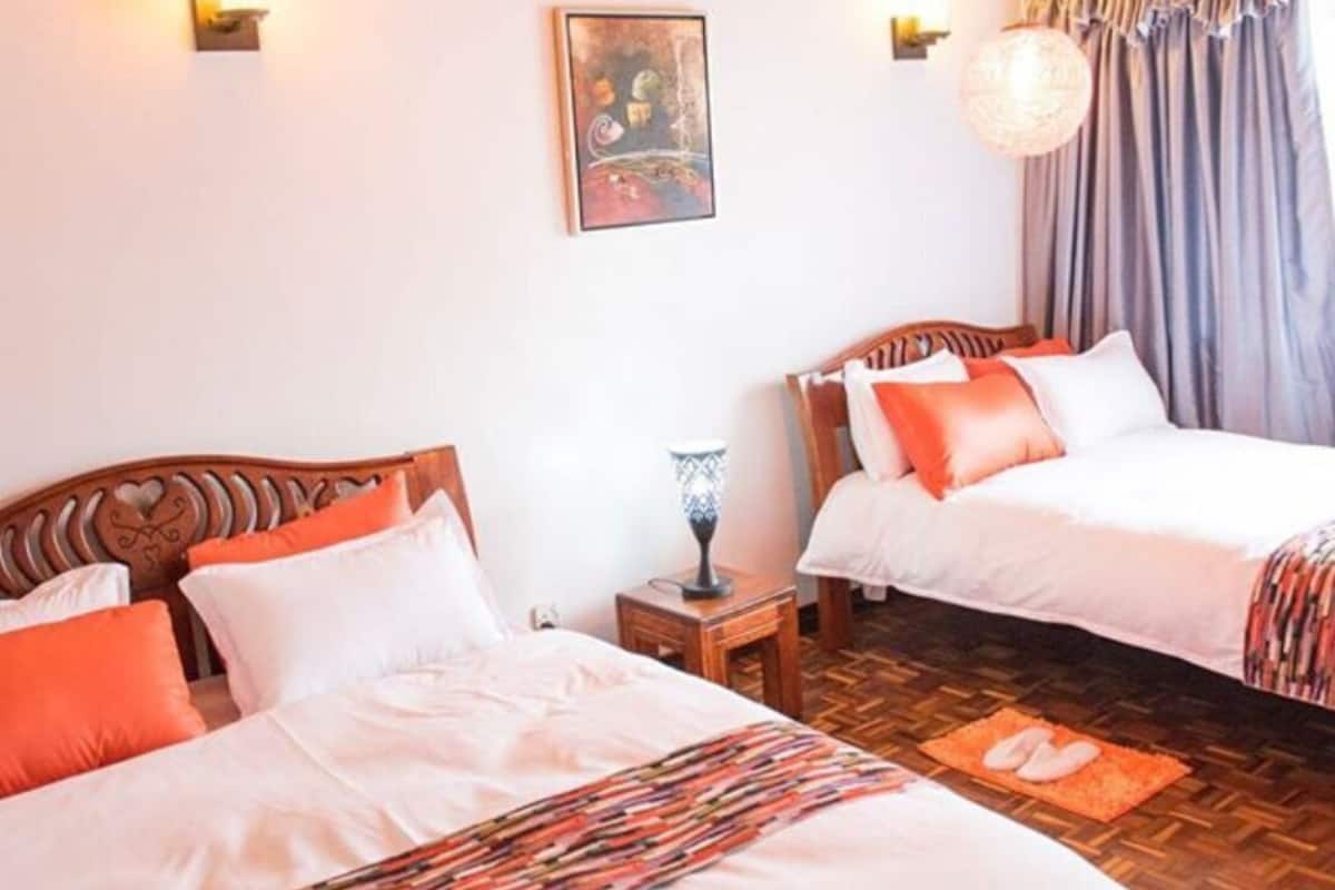 A room with two beds, wooden headboards, a wall-mounted light fixture, a hanging light, and a framed picture.