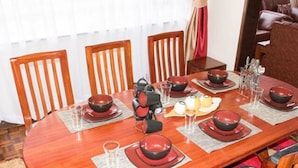 A round wooden dining table set with red and black bowls, glasses, and a teapot, surrounded by wooden chairs with grey cushions.