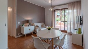 A modern living room with a white sofa, a dining table with chairs, a white cabinet, and a TV mounted on the wall. - Il Parco Apartments - Apartment with Terrace (Marina di Massa)