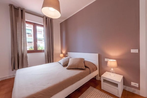 A bedroom with a bed, curtains, a bedside lamp, and a window.
