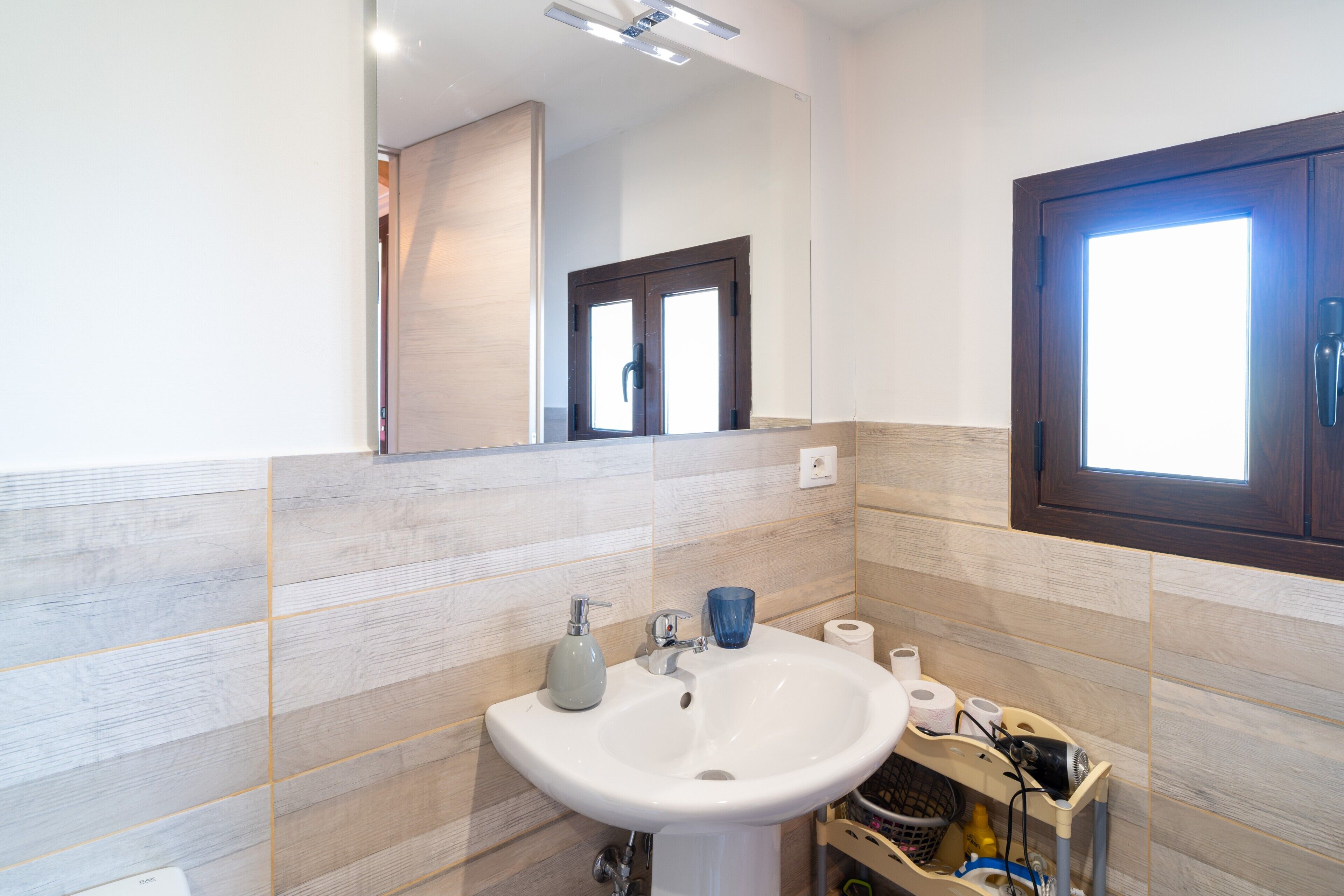 Un baño con un lavabo blanco, un espejo y una pared de madera.