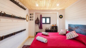 Een slaapkamer met een houten plafond, een bed met rode beddengoed, twee kussens, een hoofdbord en een kapstok aan de muur.