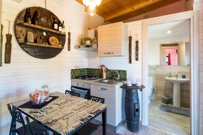 A kitchen with wooden shelves, a dining table with newspaper print, and a sink. - Holiday Home with Wi-Fi, Air Conditioning, Garden and Jacuzzi (PIEDIMONTE ETNEO)