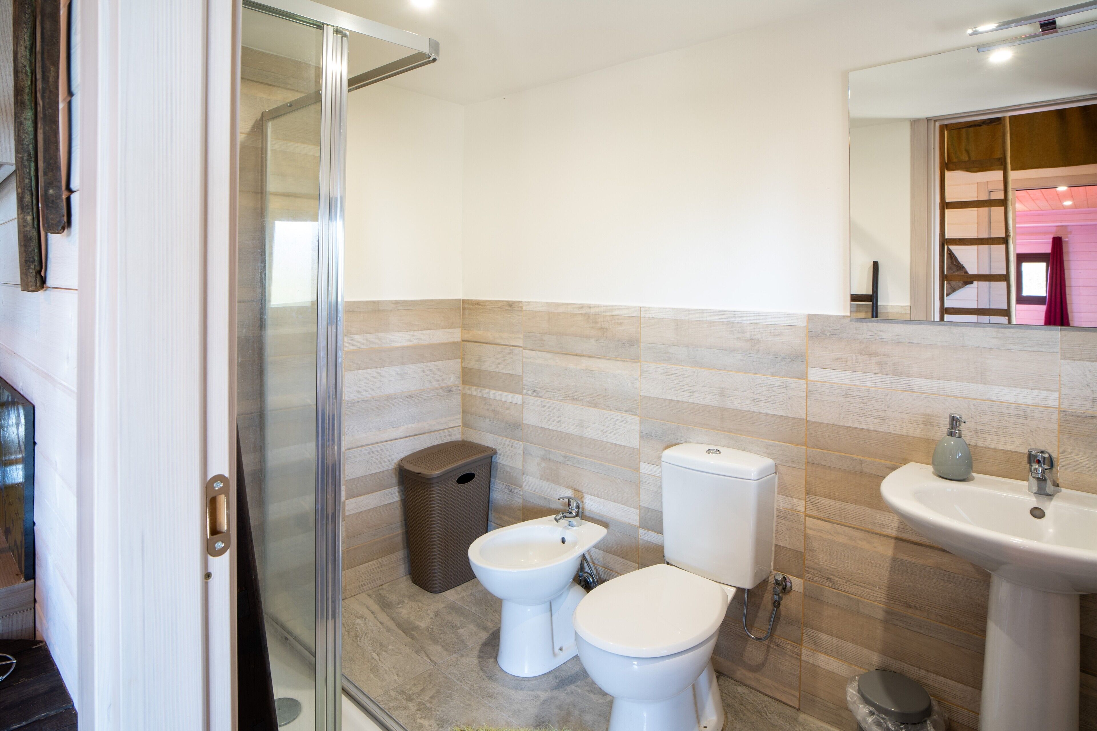 Ein Badezimmer mit Duschabtrennung aus Glas, einem Bidet, einer Toilette, einem Waschbecken und einem Mülleimer.