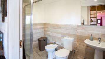Ein Badezimmer mit Duschabtrennung aus Glas, einem Bidet, einer Toilette, einem Waschbecken und einem Mülleimer.