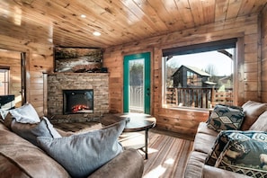 Interior acogedor de una cabaña con chimenea de piedra, paredes de madera y una puerta verde que da al exterior.