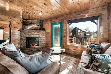 A cozy cabin interior with a stone fireplace, wooden walls, and a green door leading outside.