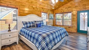 Un dormitorio de cabaña de madera con cama, mesitas de noche y ventilador de techo.
