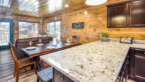 Interior de una cabaña de madera con comedor, cocina y un gran ventanal.
