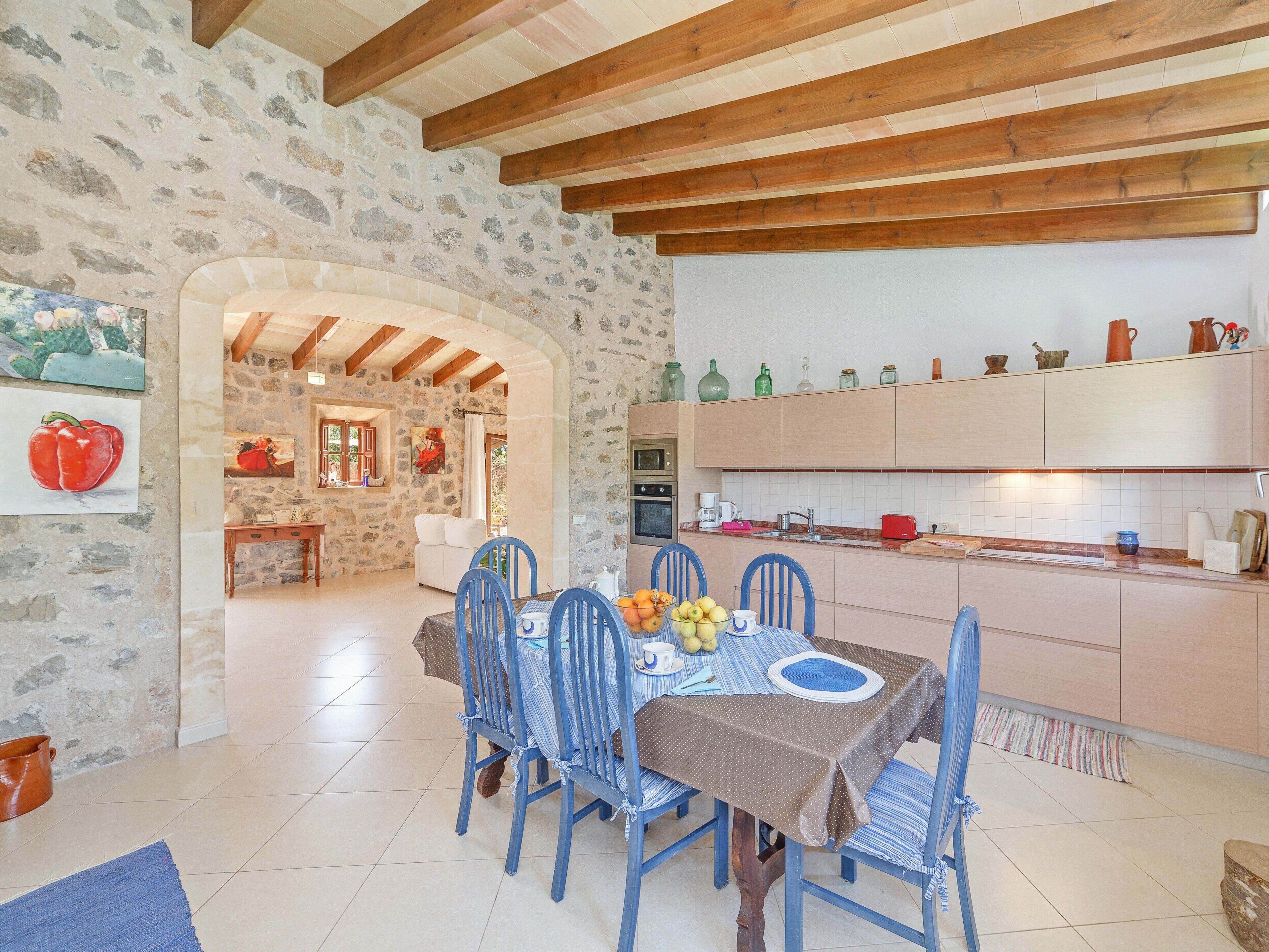 A dining area with a table set for four, a kitchen with wooden cabinets, and a stone wall.