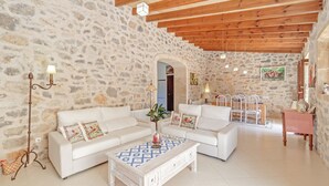 A spacious living area with stone walls, wooden beams, white furniture, and a tiled floor. - Stone-villa in a rural idyll with pool– Villa Mamici (Capdepera)