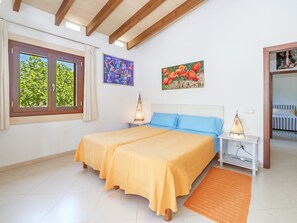Un lit double avec une literie jaune, une table de chevet avec une lampe, une fenêtre avec des rideaux et deux tableaux accrochés au mur.