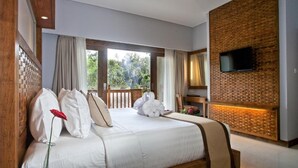 A bedroom with a large bed, a TV mounted on a brick wall, and a balcony with curtains. - Private room in a valley of Ubud, feel the tranquility of Ubud by the river (Ubud)
