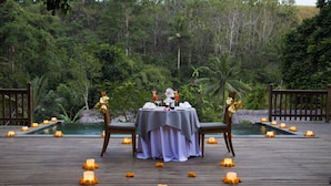 A wooden deck with a table set for two, surrounded by candles and flowers, overlooking a pool and lush greenery. - Private room in a valley of Ubud, feel the tranquility of Ubud by the river (Ubud)