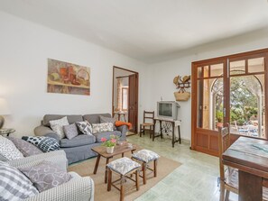 A living room with a sofa, a coffee table, a TV, and a dining area with chairs and a table.