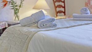 Una cama bien hecha con toallas dobladas, una lámpara, una silla y un cuadro en la pared.