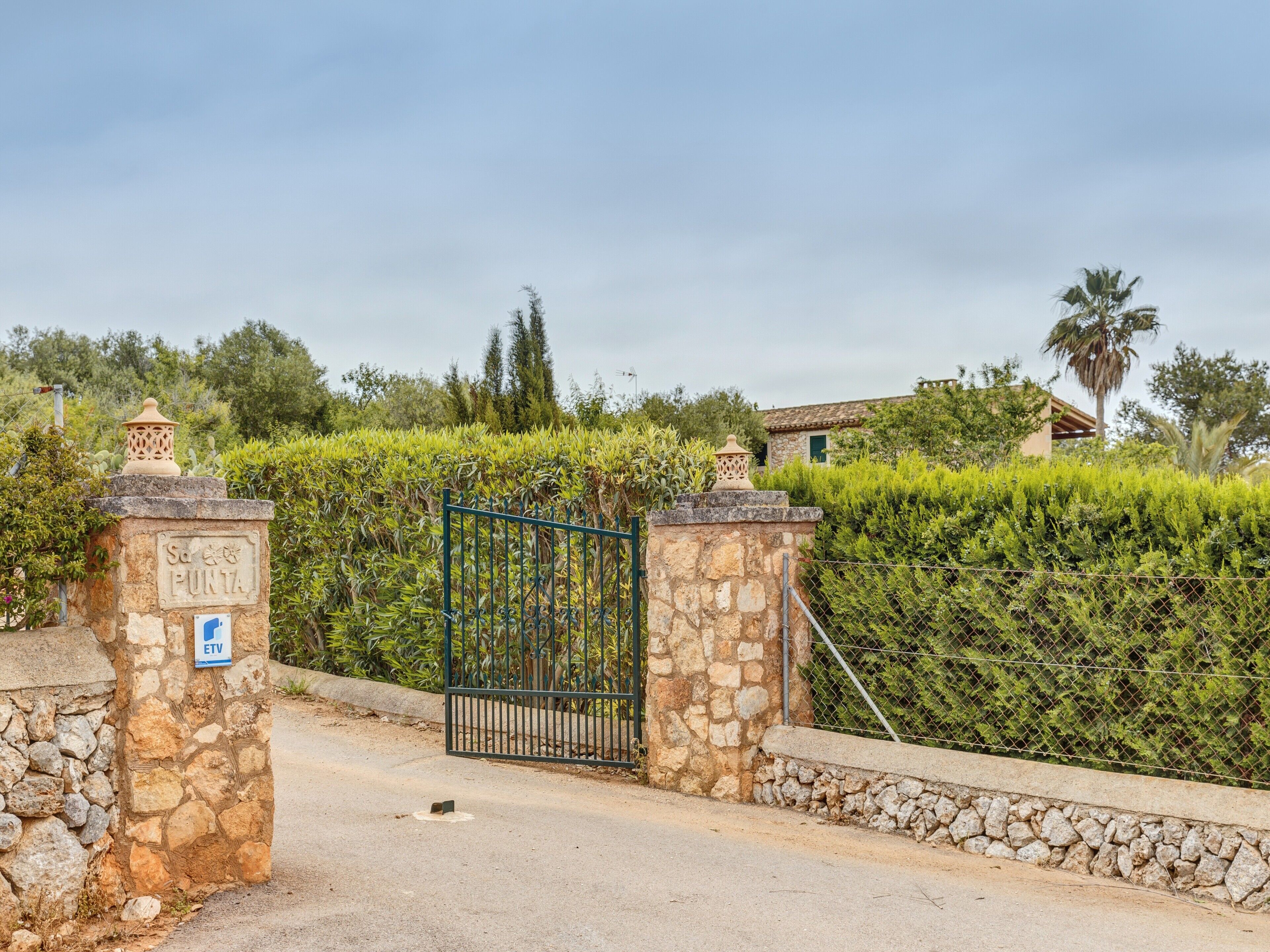 A stone gate with a metal gate, a sign reading 'Sa Punta,' and a blue ETV parking sign.